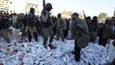 مقاتلون من تنظيم الدولة الإسلامية يحملون أسلحتهم ويقفون على عبوات سجائر مصادرة قبل حرقها، الرقة، سوريا، 2 أبريل 2014. رويترز، صحفي محلي.